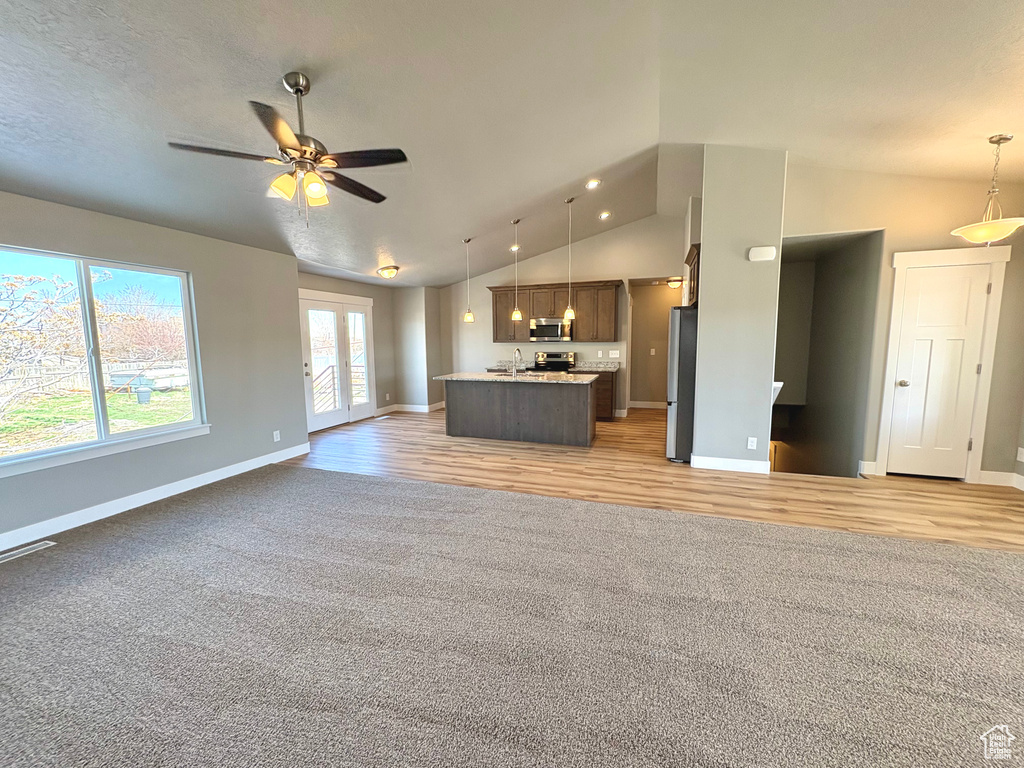 Unfurnished living room featuring vaulted ceiling, light colored carpet, ceiling fan, and light wood-type flooring