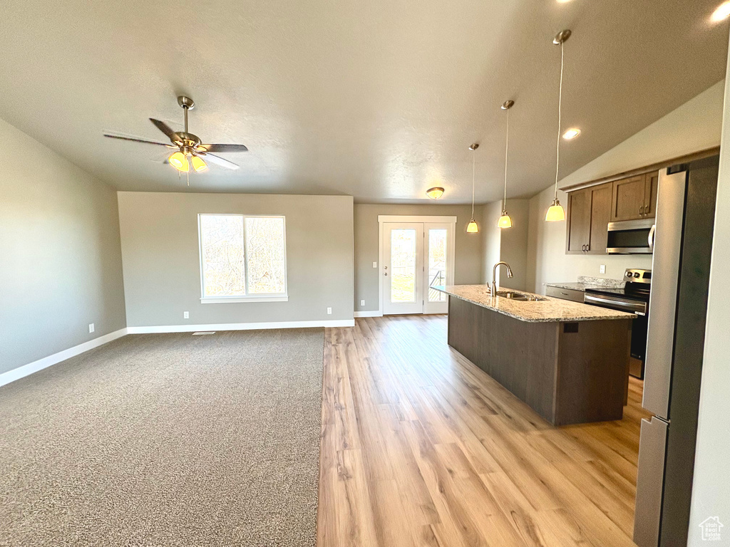 Kitchen with appliances with stainless steel finishes, a center island with sink, vaulted ceiling, a ceiling fan, and light stone counters