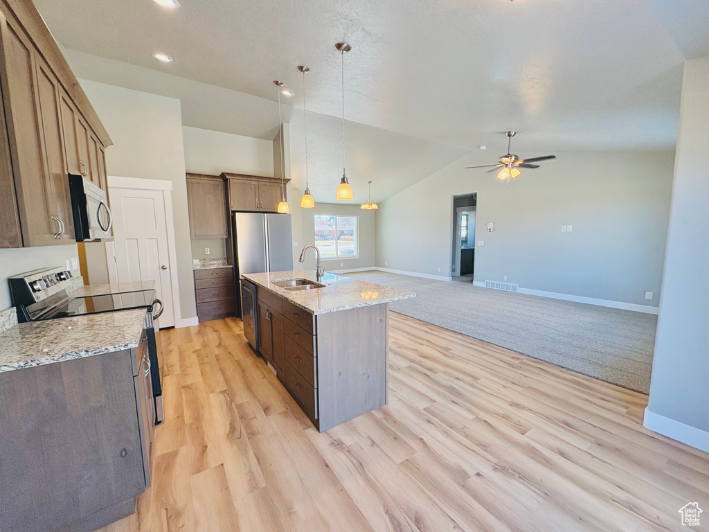 Kitchen with stainless steel appliances, vaulted ceiling, pendant lighting, light wood-style floors, and an island with sink