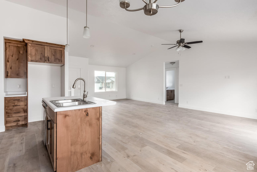 Kitchen featuring open floor plan, decorative light fixtures, brown cabinets, lofted ceiling, and light wood-style floors