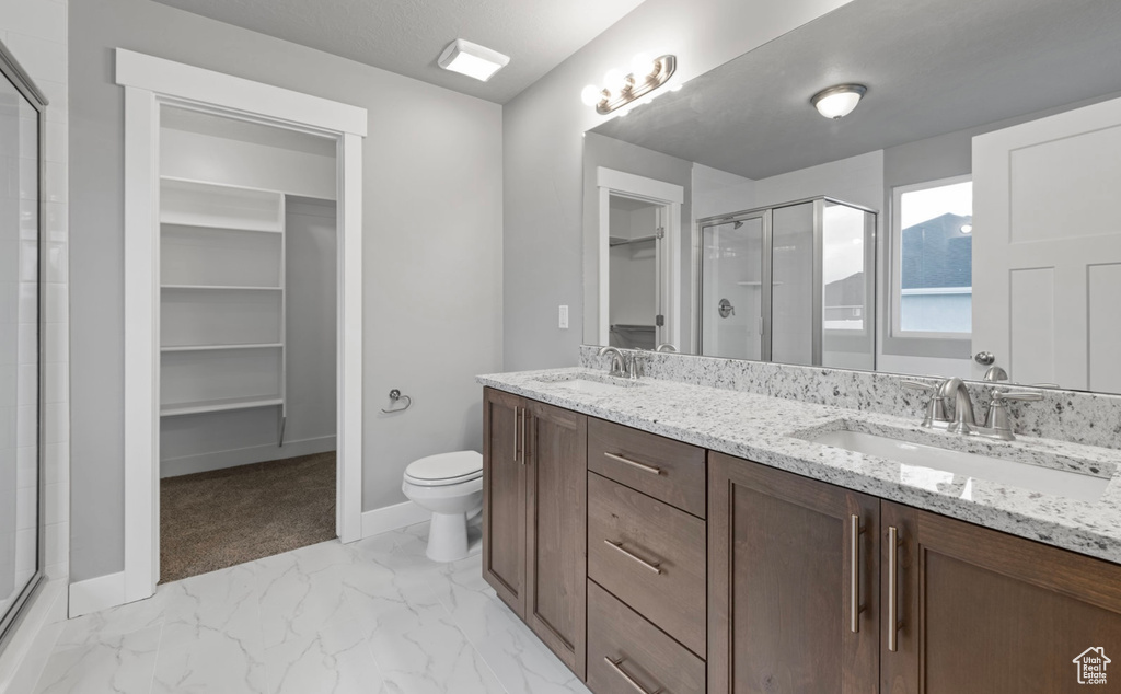 Full bath featuring a stall shower, a spacious closet, double vanity, and marble finish flooring