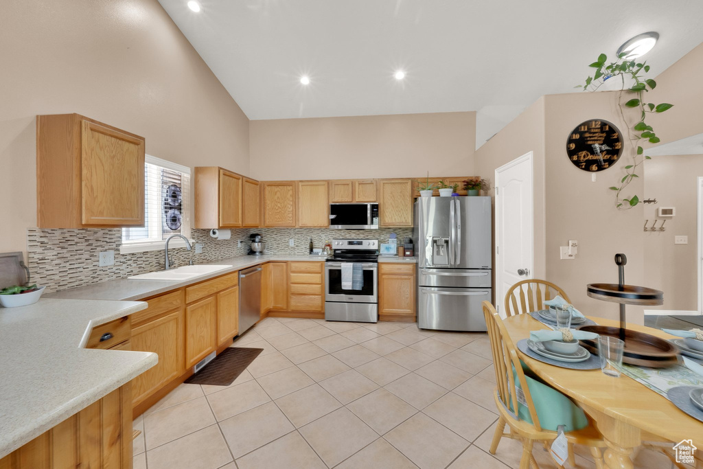 Kitchen with appliances with stainless steel finishes, backsplash, light countertops, light brown cabinets, and high vaulted ceiling