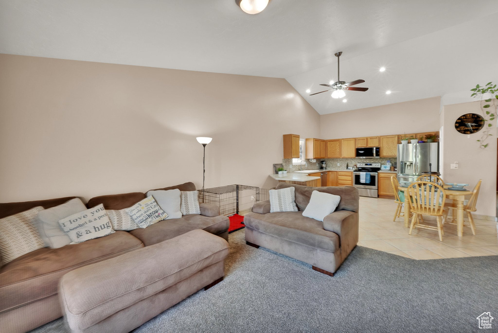 Living room featuring a ceiling fan, light tile patterned floors, high vaulted ceiling, and light colored carpet