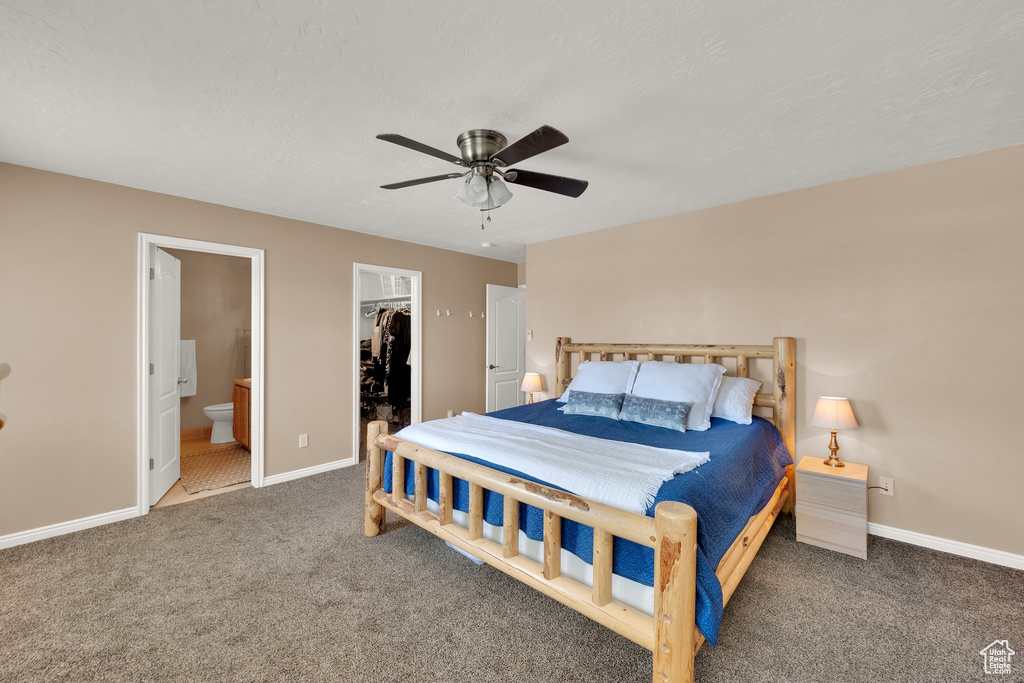 Carpeted bedroom featuring a walk in closet, ensuite bathroom, a closet, and ceiling fan