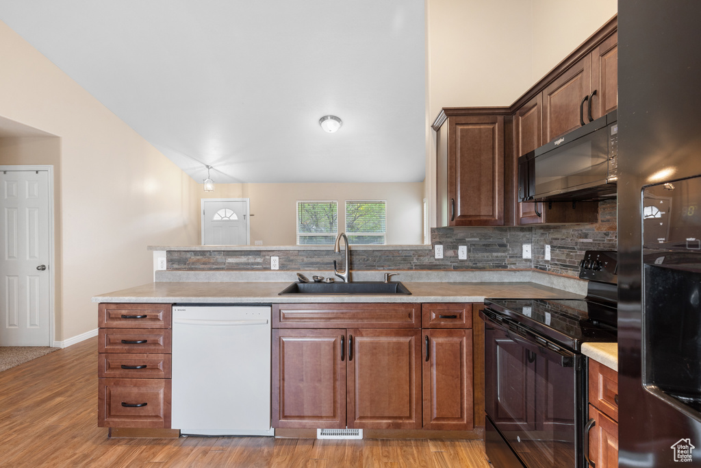Kitchen with black appliances, backsplash, light wood-style floors, light countertops, and lofted ceiling