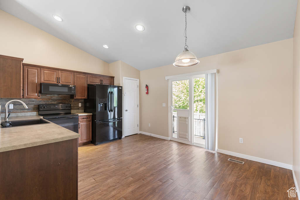Kitchen featuring black appliances, light countertops, decorative backsplash, vaulted ceiling, and light wood-type flooring