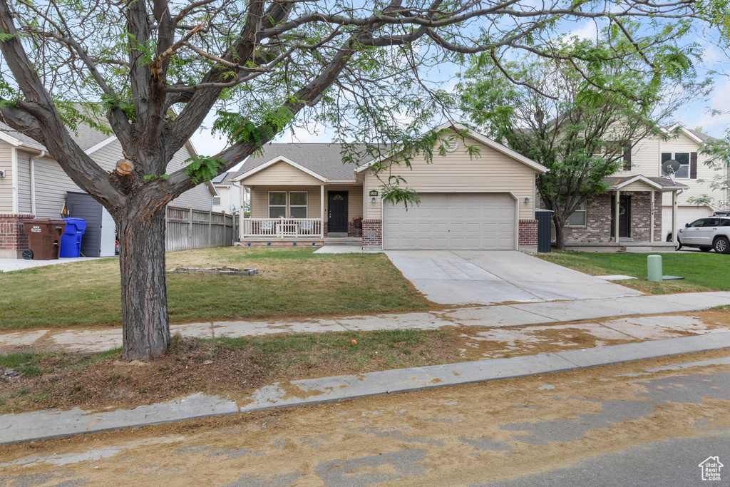 View of front of property with a porch, an attached garage, brick siding, driveway, and a front yard