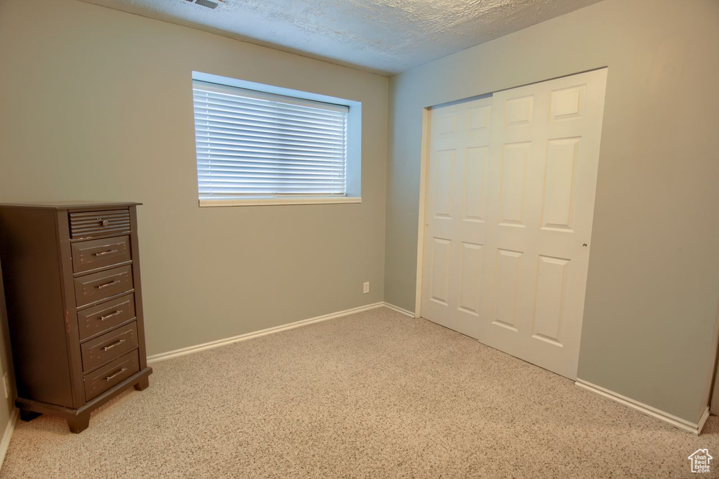 Unfurnished bedroom featuring light carpet, a closet, and a textured ceiling