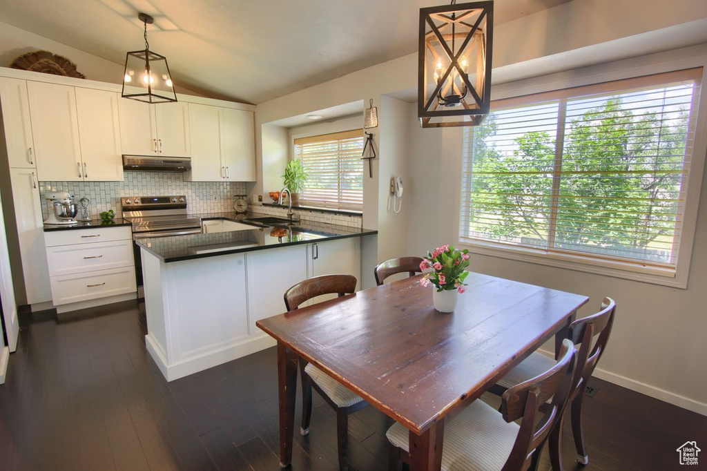 Kitchen with under cabinet range hood, tasteful backsplash, dark countertops, lofted ceiling, and white cabinetry