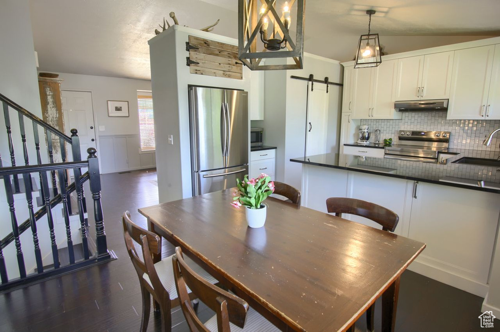 Dining space with a barn door, dark wood-style floors, stairs, and wainscoting