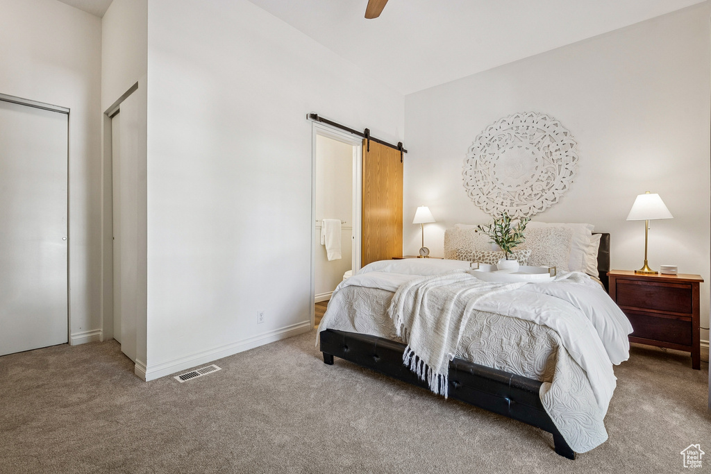 Bedroom featuring a barn door, carpet flooring, ensuite bath, and ceiling fan