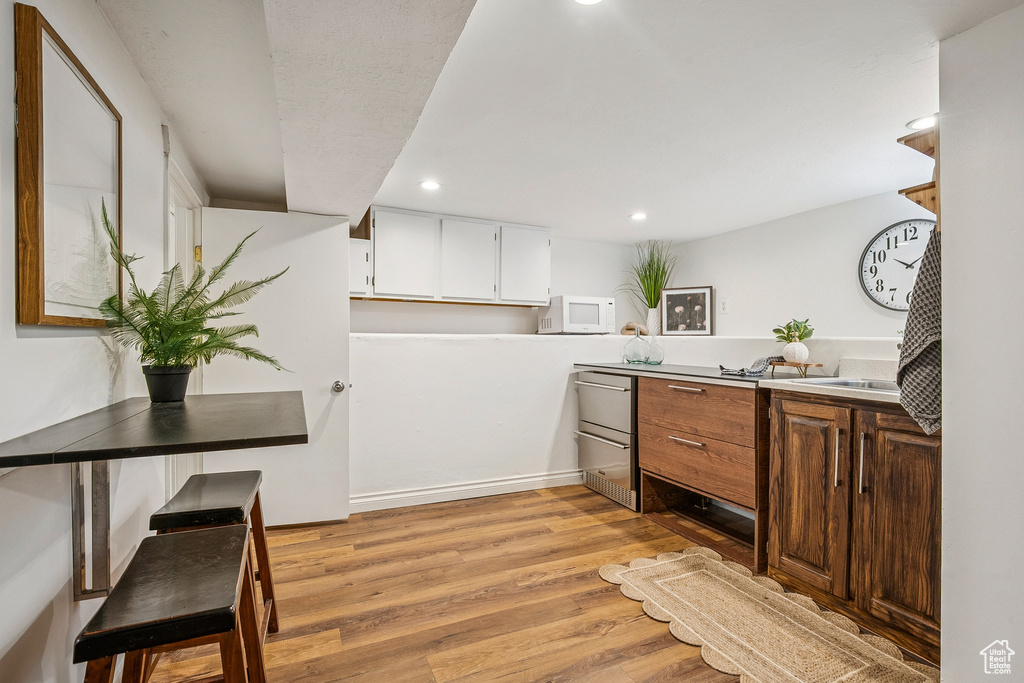 Kitchen featuring white microwave, light wood-style floors, recessed lighting, white cabinetry, and light countertops