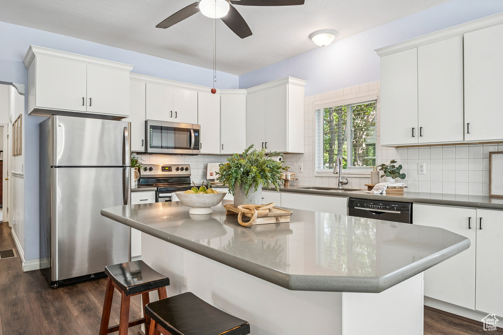 Kitchen featuring appliances with stainless steel finishes, dark wood-style floors, ceiling fan, a kitchen breakfast bar, and tasteful backsplash