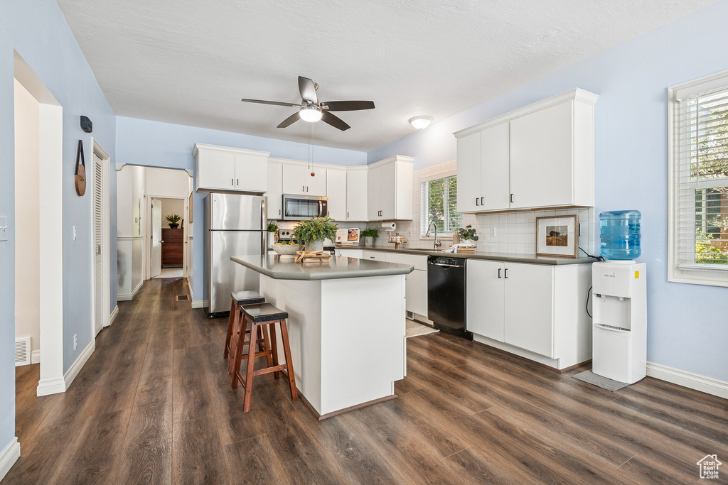 Kitchen with stainless steel appliances, dark wood-style floors, ceiling fan, and decorative backsplash