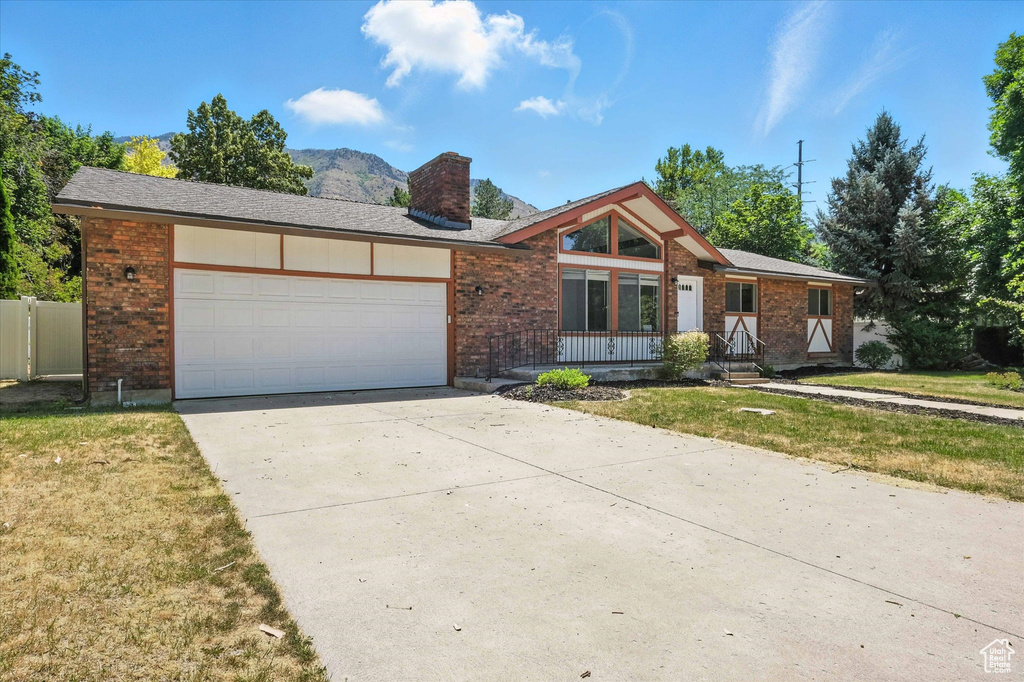 View of front of property featuring a chimney, brick siding, an attached garage, driveway, and a front yard
