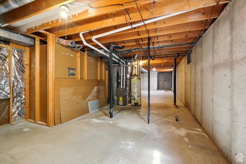 Unfinished below grade area featuring strapped water heater and heating unit