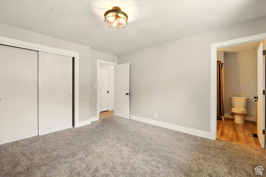 Unfurnished bedroom featuring light colored carpet, a closet, and ensuite bath