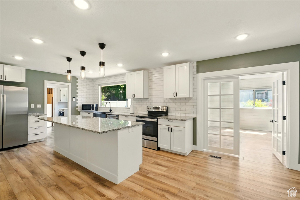 Kitchen with stainless steel appliances, white cabinets, light wood-style flooring, tasteful backsplash, and a center island