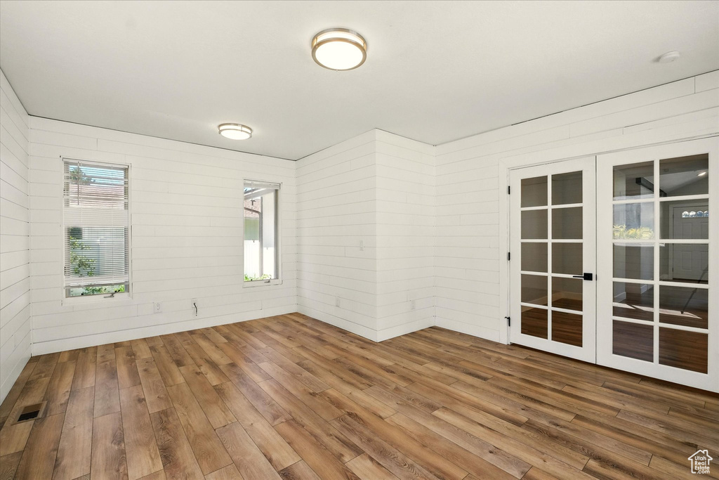 Empty room with french doors, hardwood / wood-style floors, and wooden walls