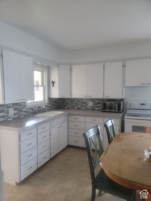 Kitchen featuring white range with electric stovetop, a sink, tasteful backsplash, and white cabinetry