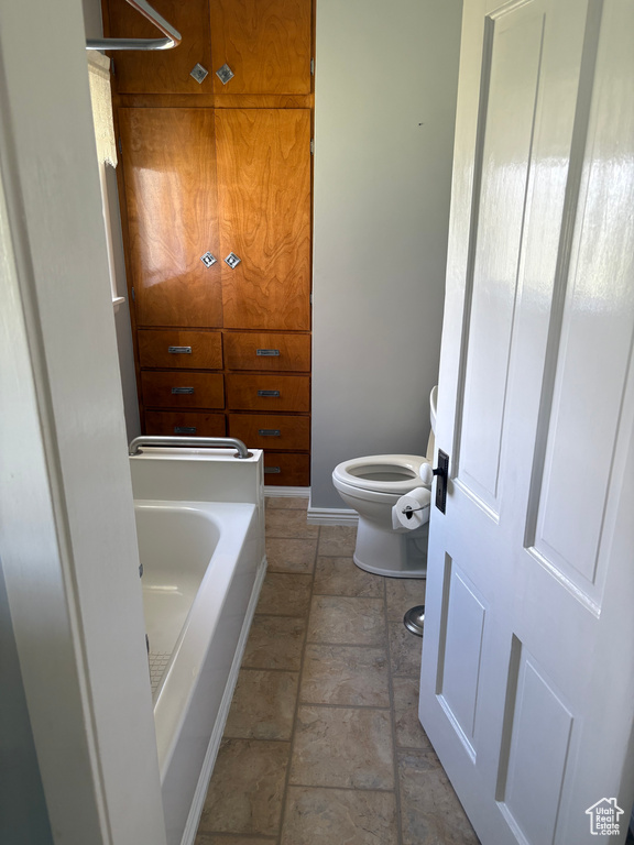 Full bath featuring toilet, a tub to relax in, and baseboards