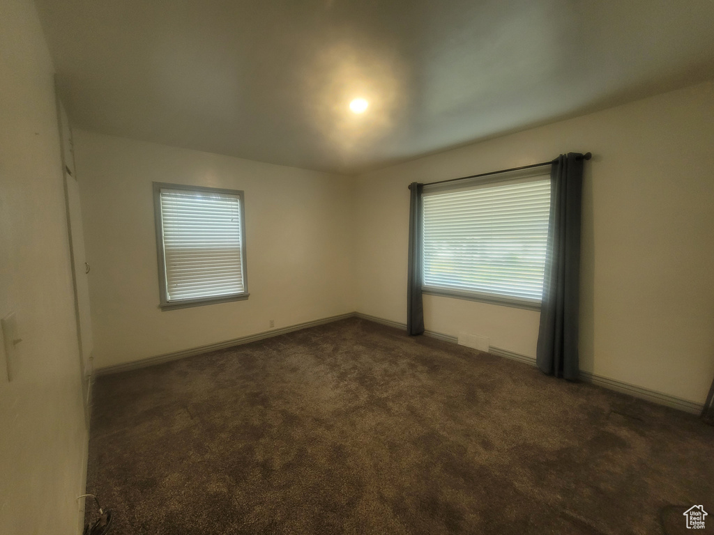 Spare room featuring dark colored carpet and baseboards