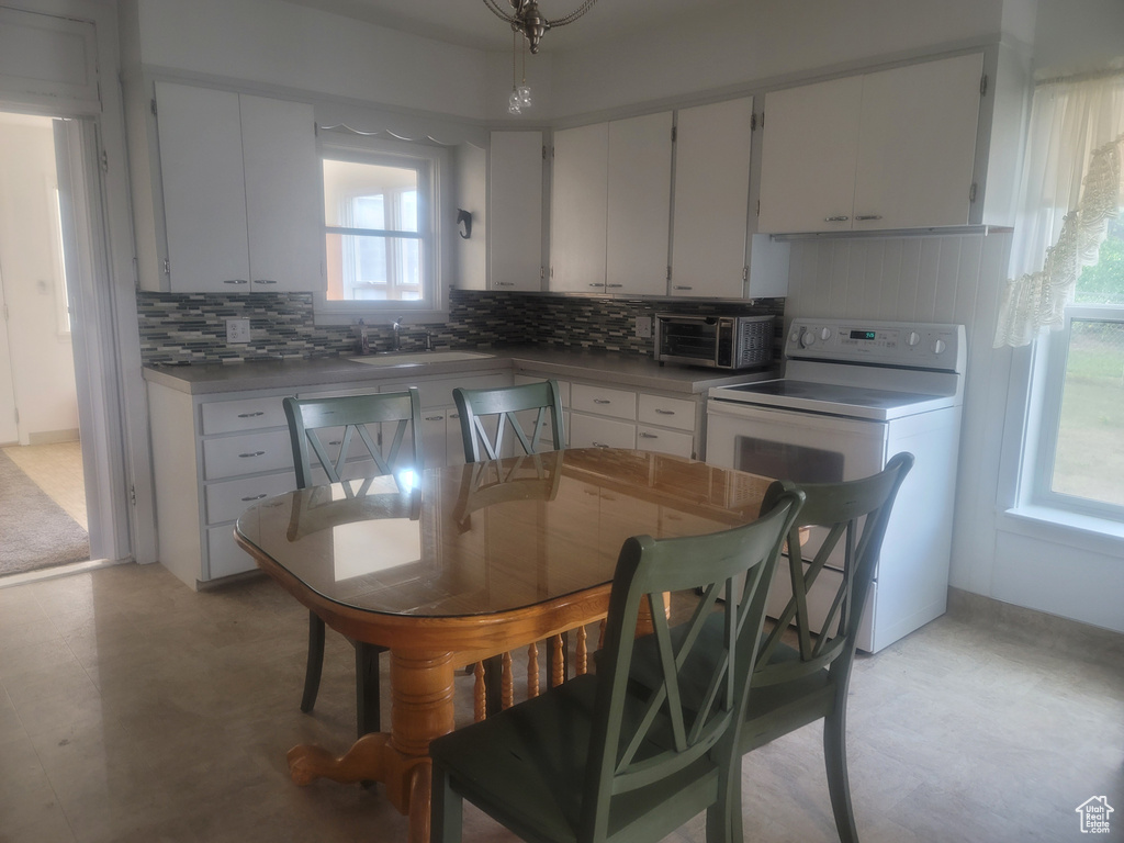 Kitchen with stove, tasteful backsplash, a sink, white cabinetry, and light floors