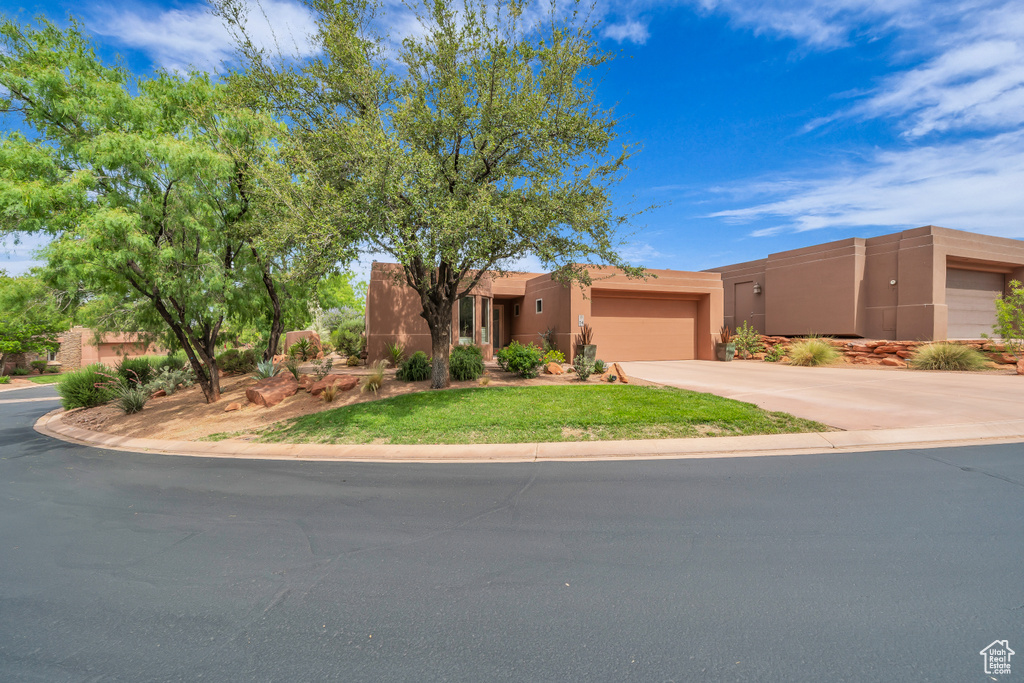 Adobe home featuring an attached garage, driveway, stucco siding, and a front lawn