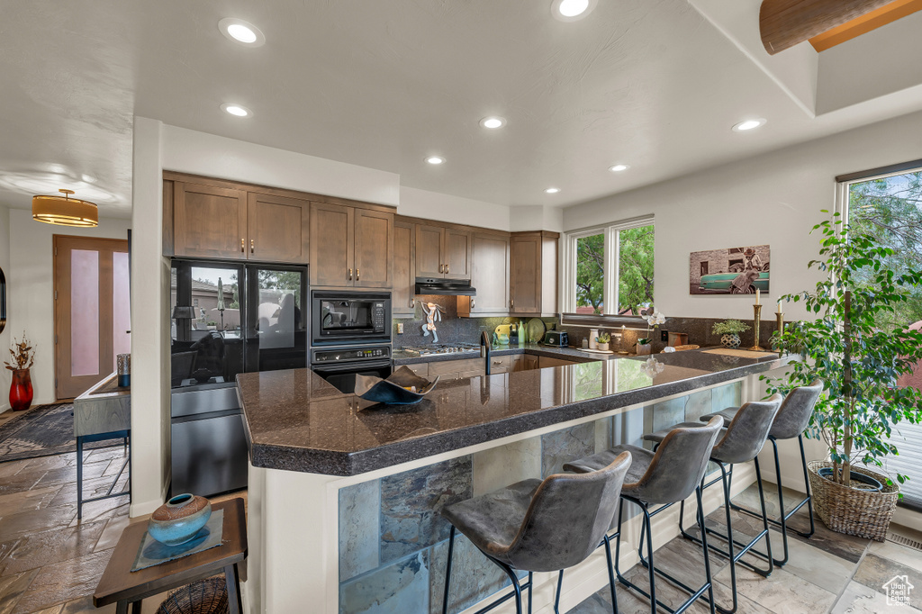 Kitchen featuring black appliances, recessed lighting, exhaust hood, a breakfast bar area, and plenty of natural light