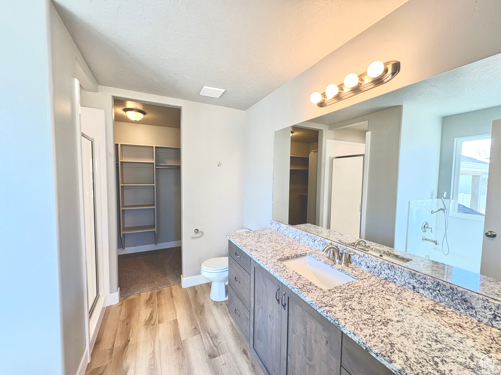 Full bathroom featuring a stall shower, a spacious closet, vanity, wood finished floors, and a textured ceiling