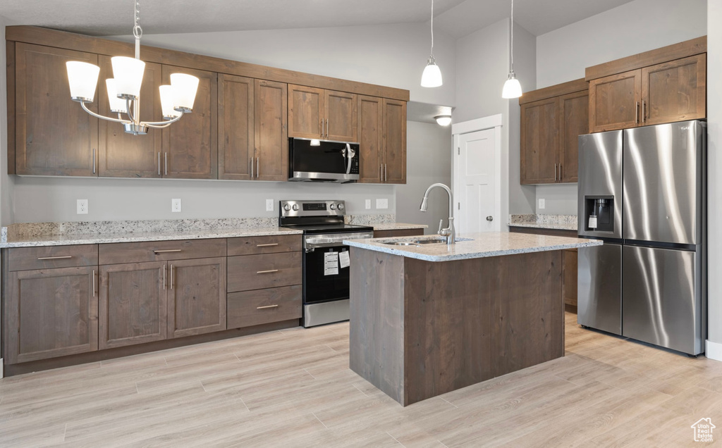 Kitchen featuring stainless steel appliances, decorative light fixtures, light stone counters, a chandelier, and high vaulted ceiling