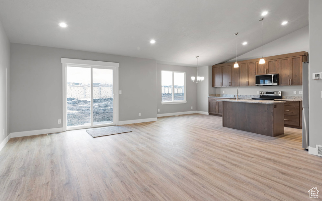 Kitchen featuring appliances with stainless steel finishes, open floor plan, light wood-style floors, a center island with sink, and recessed lighting