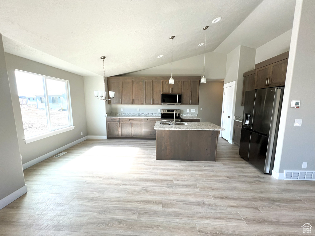 Kitchen featuring appliances with stainless steel finishes, vaulted ceiling, an island with sink, light wood-style flooring, and pendant lighting