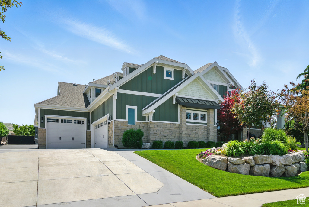 Craftsman-style house with board and batten siding, stone siding, an attached garage, a front yard, and concrete driveway