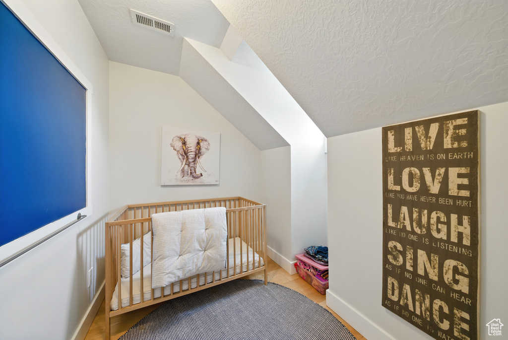 Bedroom featuring vaulted ceiling, a nursery area, a textured ceiling, and wood finished floors