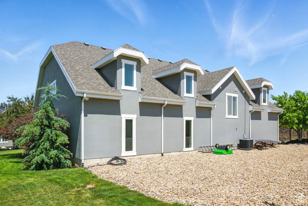 Rear view of property featuring a shingled roof, stucco siding, and a yard