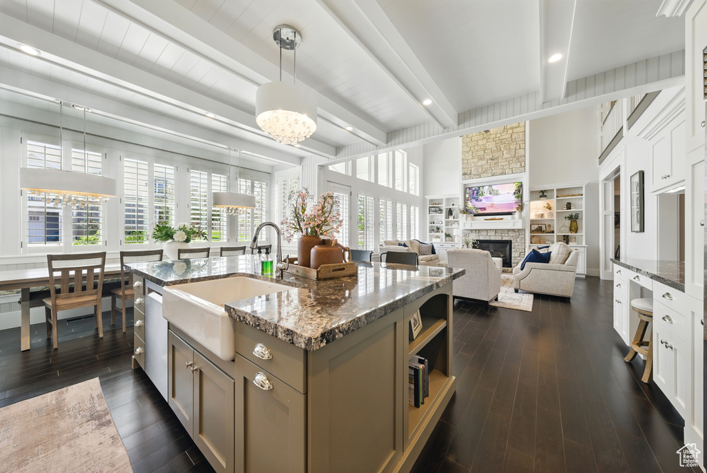 Kitchen with dishwasher, beam ceiling, dark stone counters, a fireplace, and pendant lighting