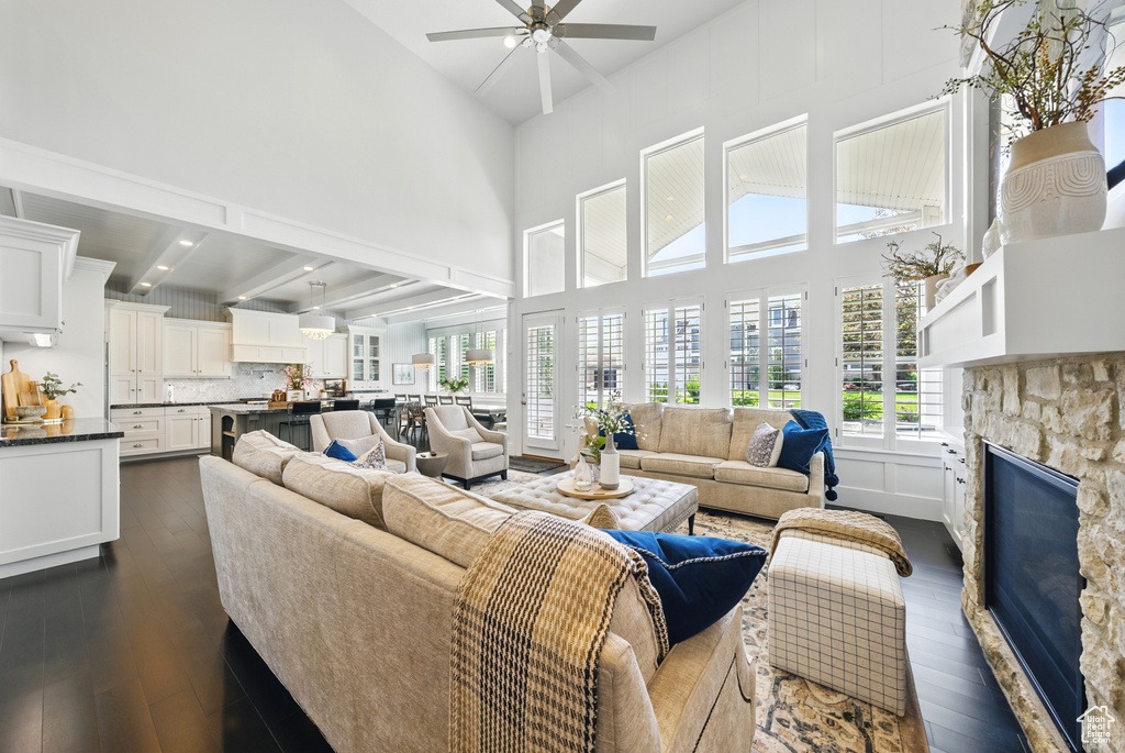 Living room featuring a towering ceiling, a ceiling fan, a fireplace, and dark wood-type flooring