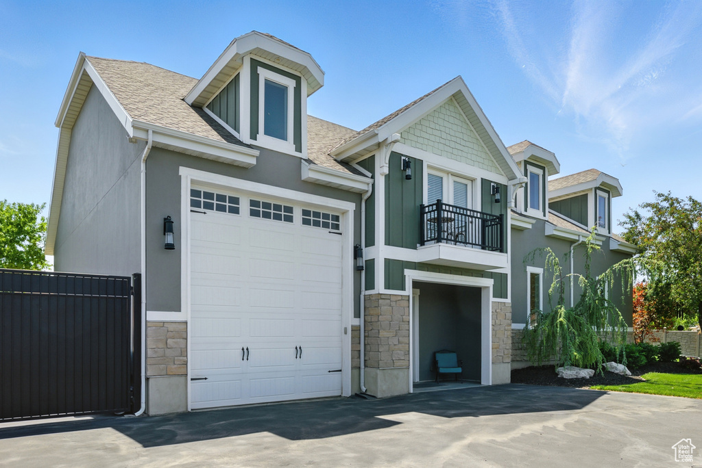 View of front of property featuring stone siding, a balcony, a garage, a shingled roof, and stucco siding