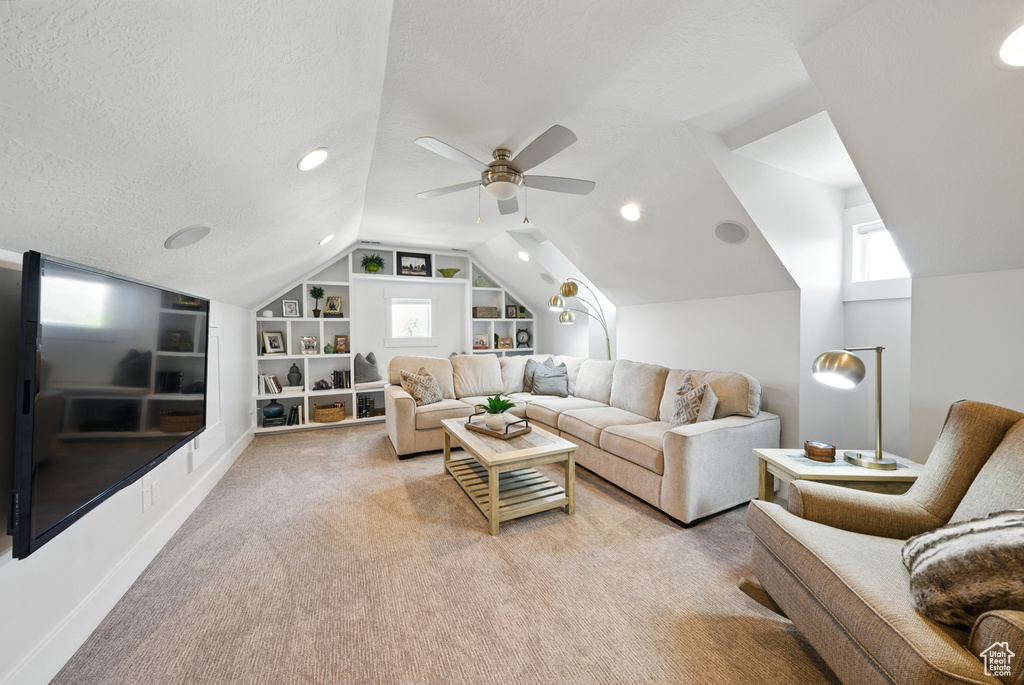 Living area with built in shelves, vaulted ceiling, light carpet, a ceiling fan, and a textured ceiling