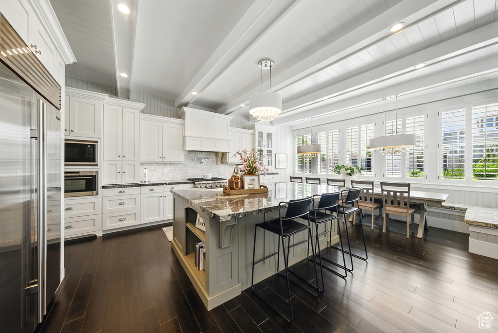 Kitchen with stainless steel appliances, beam ceiling, decorative backsplash, light stone counters, and a breakfast bar
