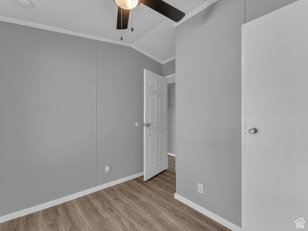 Unfurnished bedroom featuring crown molding, lofted ceiling, wood finished floors, and a ceiling fan
