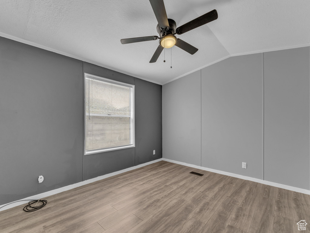 Unfurnished room featuring wood finished floors, a ceiling fan, vaulted ceiling, and crown molding