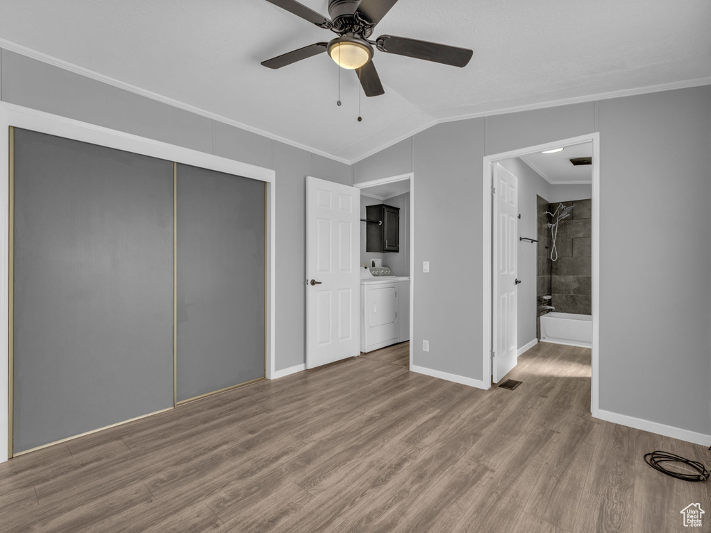 Unfurnished bedroom featuring washer / clothes dryer, crown molding, wood finished floors, vaulted ceiling, and a closet