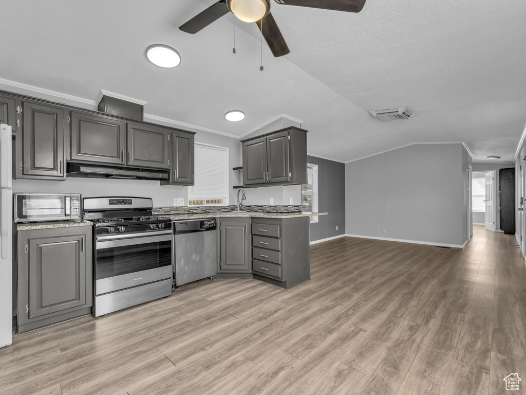 Kitchen with stainless steel appliances, under cabinet range hood, vaulted ceiling, open floor plan, and light countertops