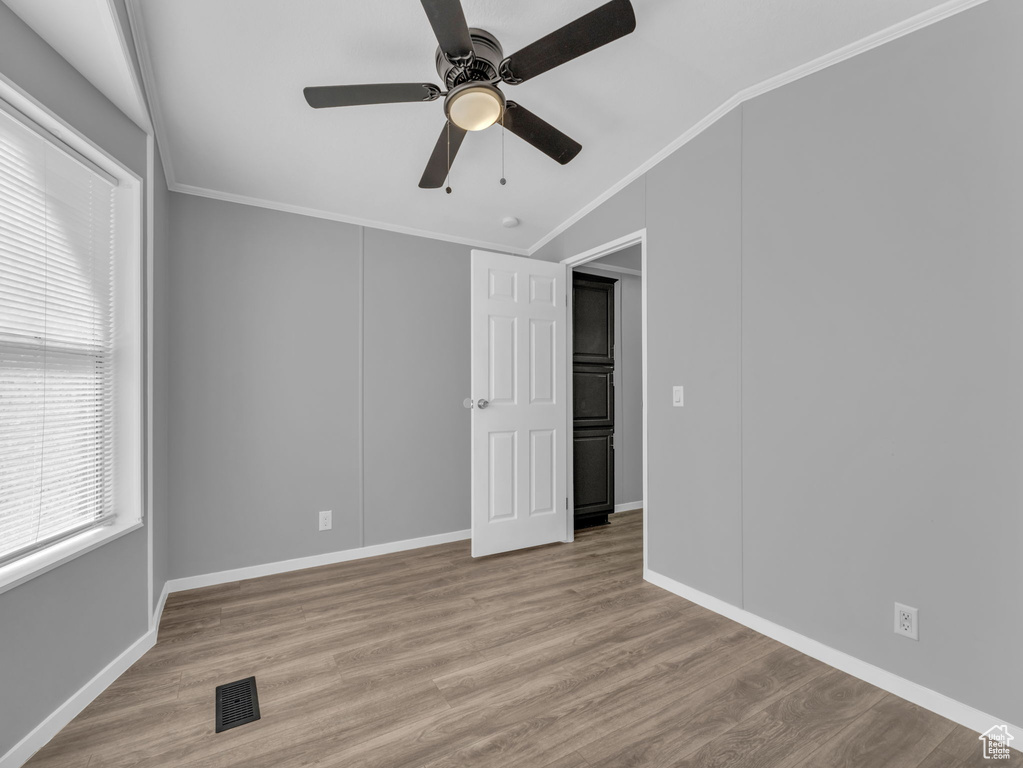 Empty room featuring vaulted ceiling, crown molding, wood finished floors, and ceiling fan