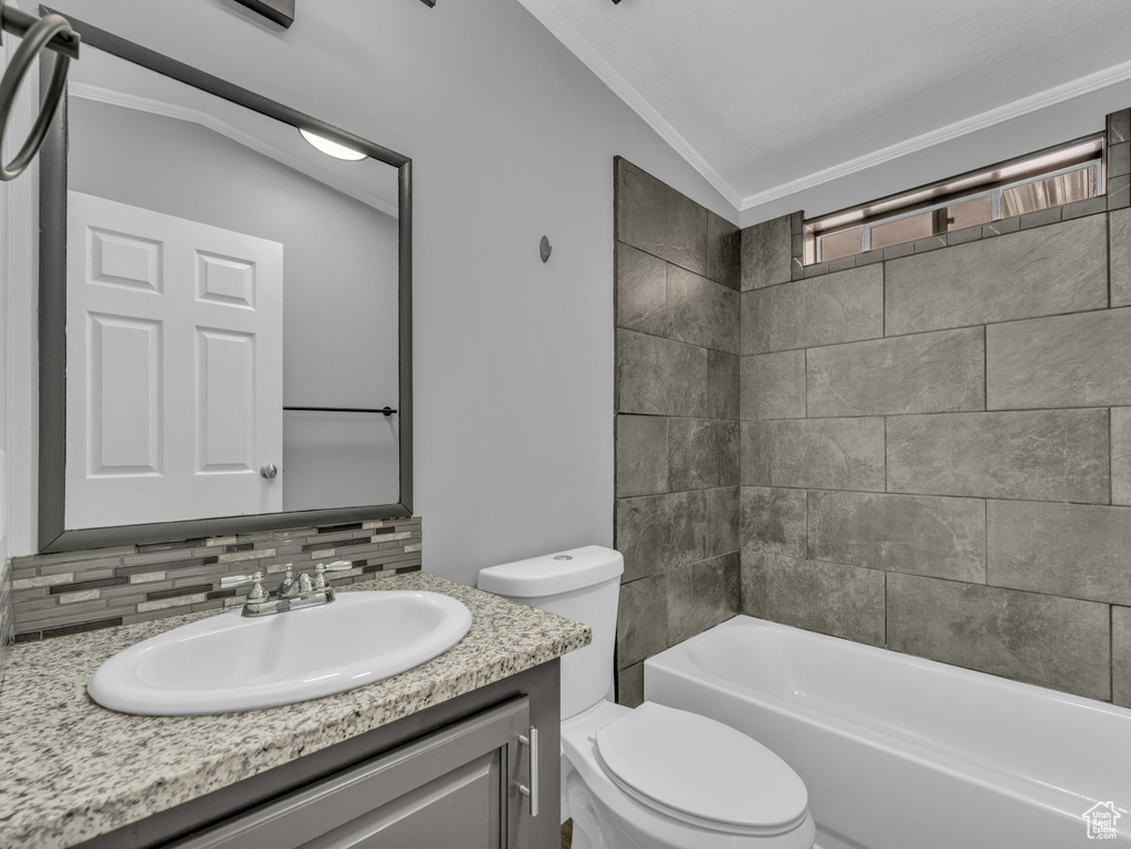 Full bath with tasteful backsplash, vanity, ornamental molding, vaulted ceiling, and washtub / shower combination