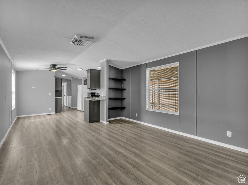 Unfurnished living room with wood finished floors, vaulted ceiling, ceiling fan, and crown molding