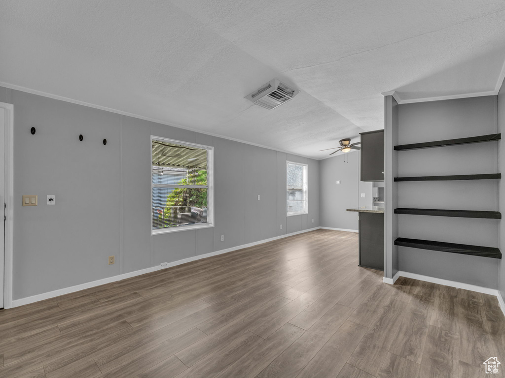 Unfurnished living room with a ceiling fan, wood finished floors, crown molding, a textured ceiling, and lofted ceiling