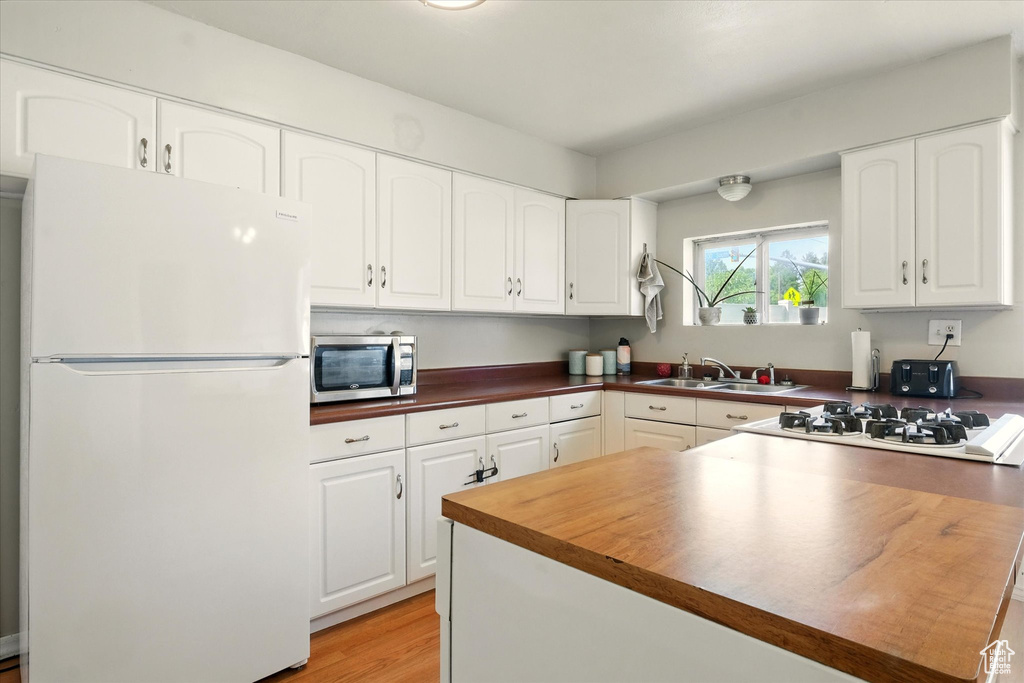 Kitchen with white appliances, white cabinetry, light wood-style flooring, and butcher block counters
